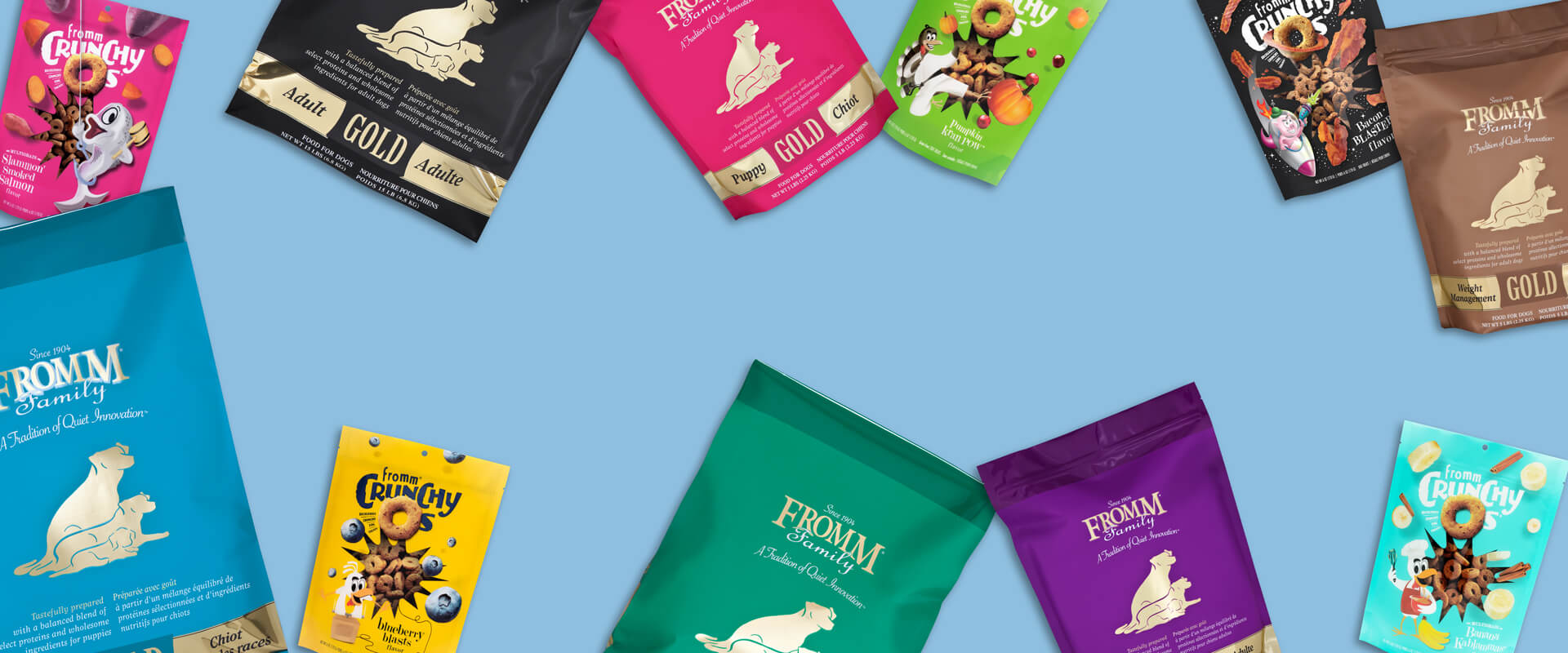 an assortment of Fromm Gold dog food and Fromm Crunchy Os dog treat bags scattered across a light blue background 
